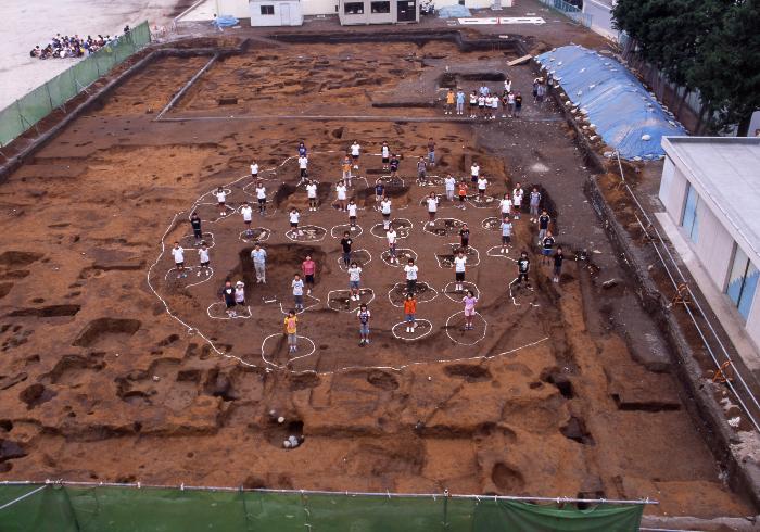 正倉跡の発掘現場に複数の小学生が立っている写真