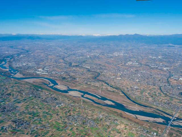伊勢崎市全体を写した航空写真です。手前に利根川が流れ、市街地を挟んだ奥には赤城山が写っています