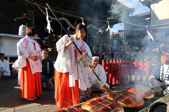 上州焼き饅祭で巫女姿の女性が巨大焼きまんじゅうに刷毛でたれを塗っている写真