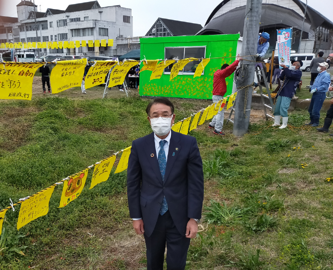 黄色いハンカチプロジェクトを訪問し、市長が掲げられたハンカチの前に立つ様子