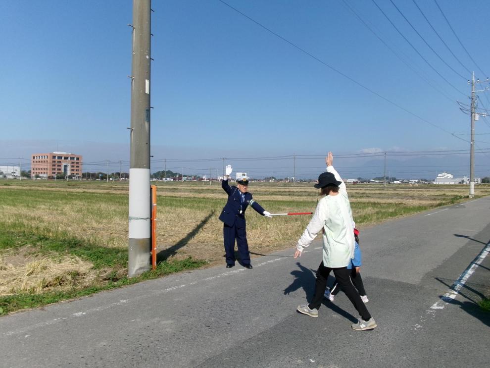 交通指導員が道路上で幼稚園児と保護者の道路横断の誘導をしています。