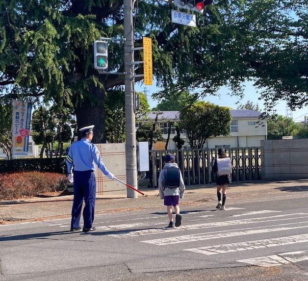 交通指導員が道路上で幼稚園児と保護者の道路横断の誘導をしています