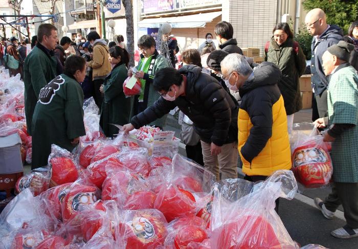 露天商の人がだるまをお客さんに売っている写真