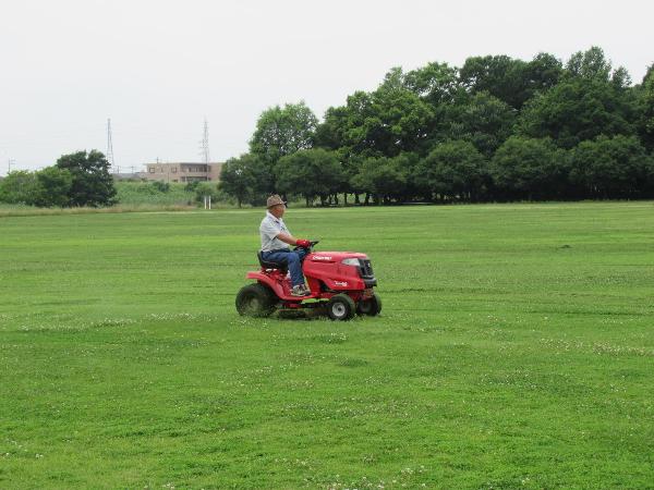 公園の芝生の上でトラクターに乗って作業する男性の様子