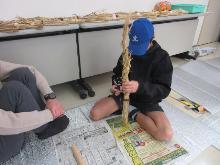 稲わらを使って、しめ縄を編んでいる子供の写真