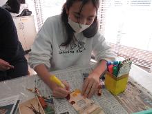 板で作った箱に模様をつけてカリンバを作っている子供の写真