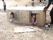 段ボールで、思い思いに形作って秘密基地を作り、お顔をのぞかせている子供の写真