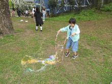 シャボン玉の液を丸いロープにつけて、大きいシャボン玉を作っている子供の写真