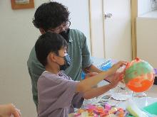 膨らませた風船に、紙をちぎって貼り付けランプシェードを作っている子供の写真