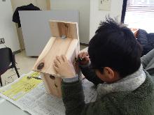 自分で作った鳥の巣箱に絵や名前を書いている子供の写真
