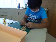 木でできたビーズをつないで、キーホルダーを作っている子供の写真