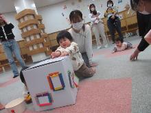 ボールやたわし等の小物の入った箱の窓から物を取り出している子供の写真